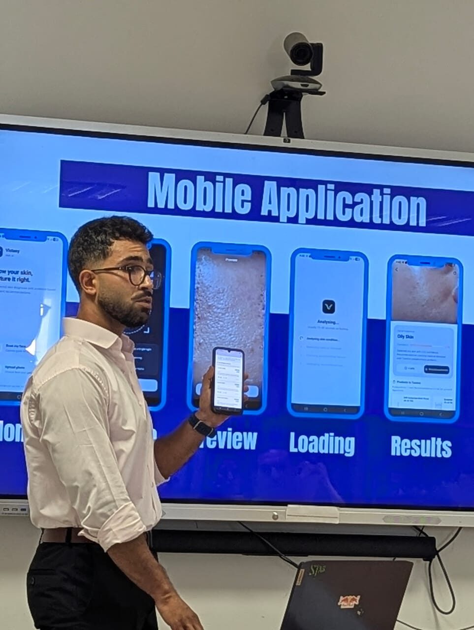 Aws Ourari presenting the Auréa mobile app screens — Preview, Loading, and Results — on a screen during a project demo